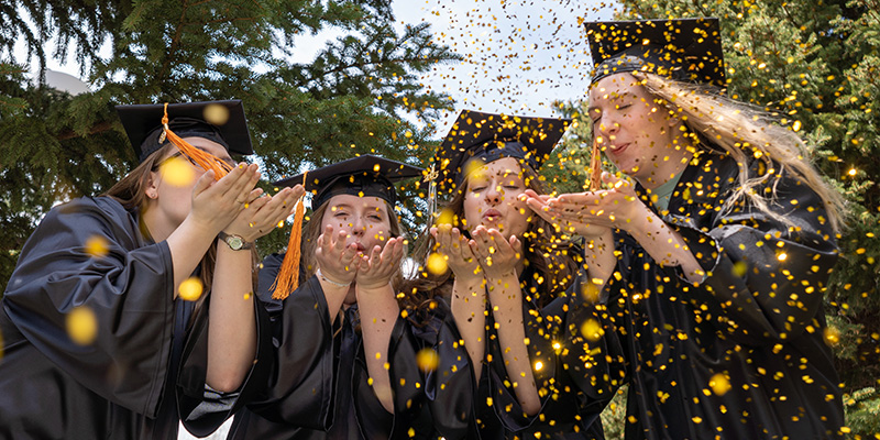 College graduates blowing glitter out of their hands
