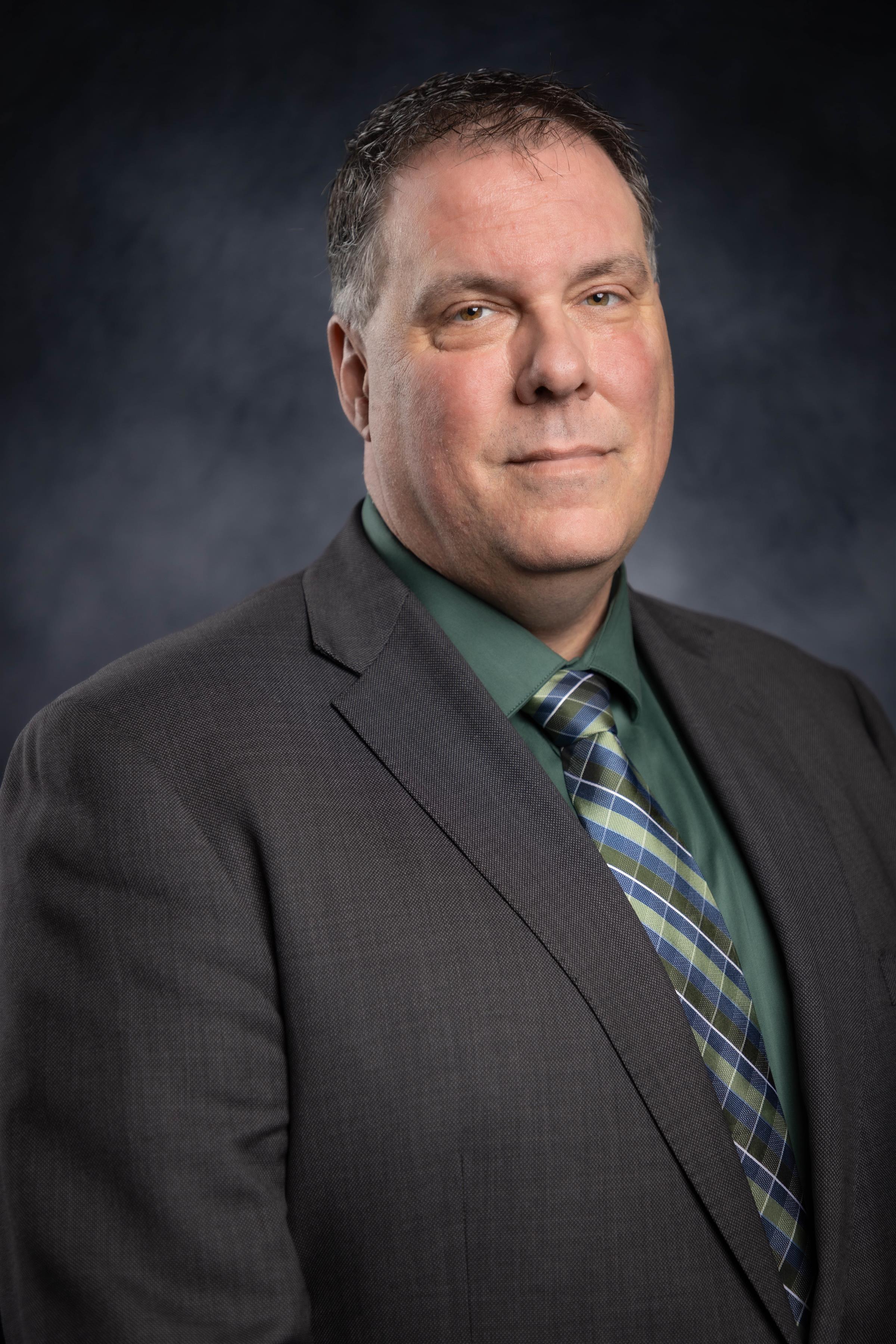 Man wearing a grey blazer with a green shirt and green plaid tie.